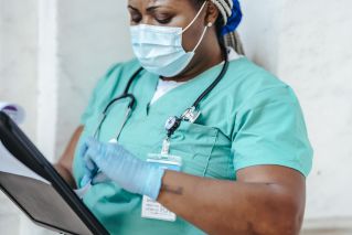 Crop African American woman in uniform standing in hospital and reading patient card while working